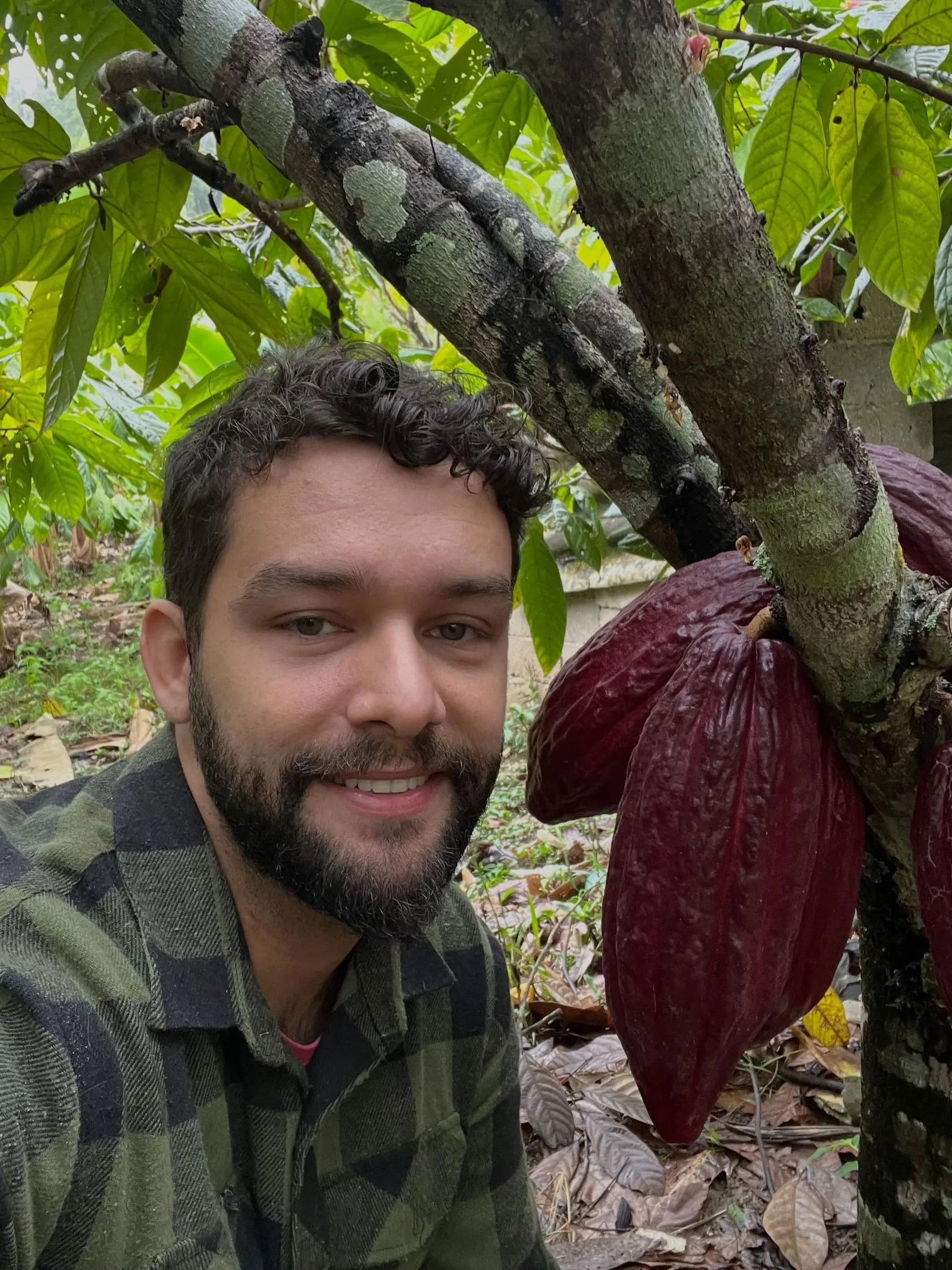 Produtor sorrindo ao lado de um fruto de cacau roxo na mata